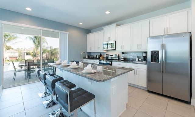 kitchen with a kitchen island with sink, white cabinetry, stainless steel appliances, dark stone counters, and a kitchen bar