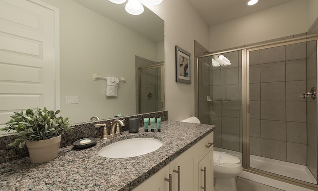 bathroom featuring a shower with shower door, vanity, and toilet