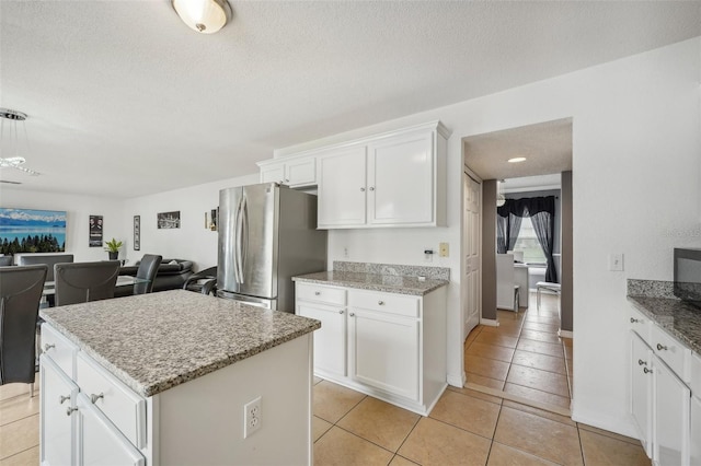 kitchen featuring a kitchen island, stainless steel fridge, light tile patterned flooring, white cabinetry, and a textured ceiling