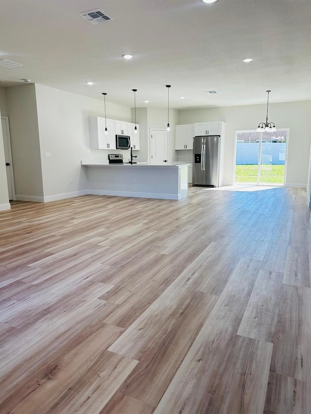 unfurnished living room featuring baseboards, recessed lighting, light wood-style flooring, a chandelier, and a sink