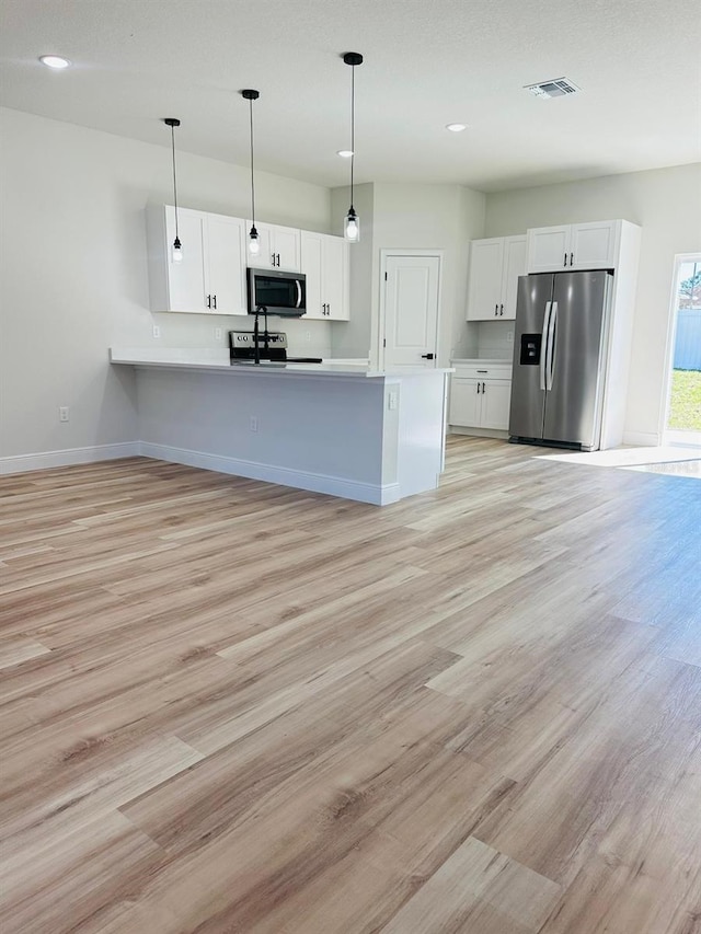 kitchen featuring appliances with stainless steel finishes, kitchen peninsula, white cabinetry, pendant lighting, and light hardwood / wood-style flooring