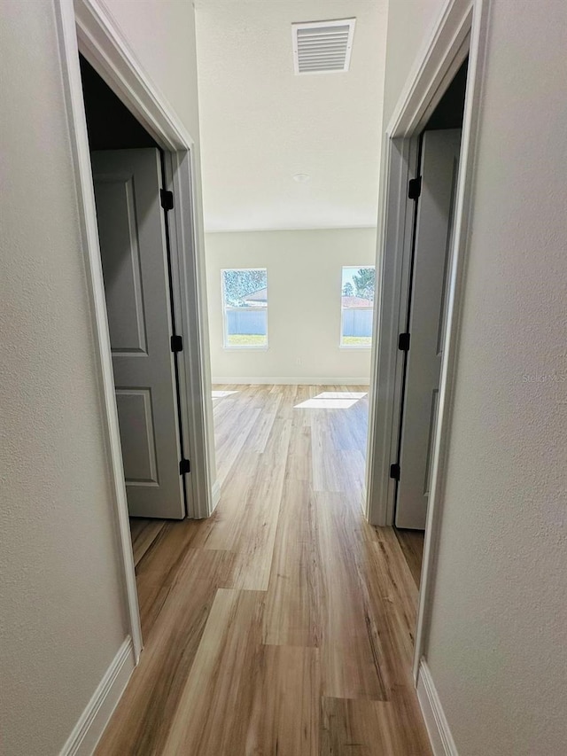 hall featuring wood finished floors, baseboards, and a textured wall
