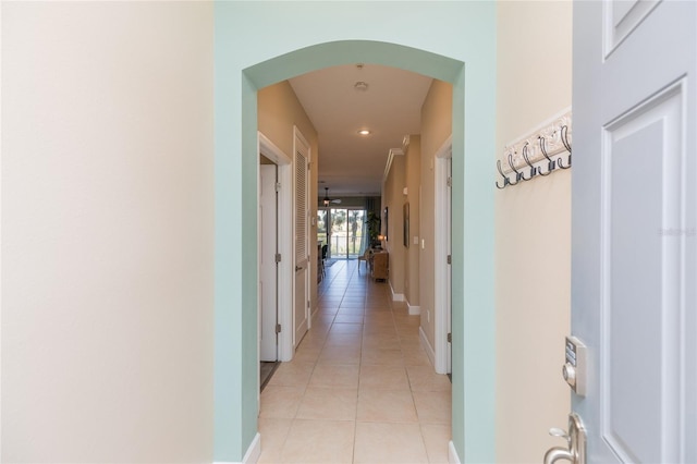 corridor with baseboards, arched walkways, and light tile patterned flooring