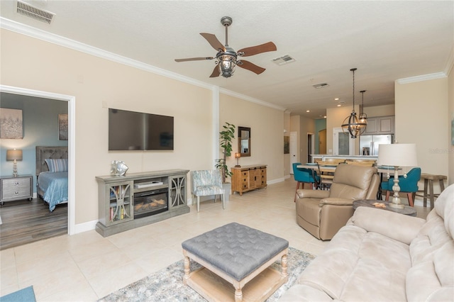 living room featuring light tile patterned floors, ornamental molding, a glass covered fireplace, and visible vents