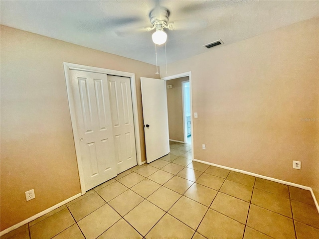 unfurnished bedroom with light tile patterned floors, ceiling fan, and a closet