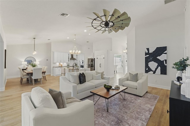 living room with ceiling fan with notable chandelier, sink, vaulted ceiling, and light wood-type flooring