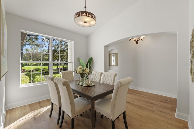 dining space with a wealth of natural light, lofted ceiling, light hardwood / wood-style flooring, and a notable chandelier