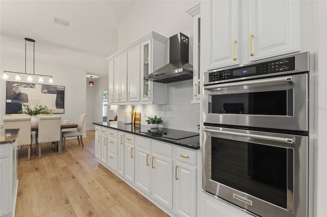 kitchen featuring backsplash, wall chimney exhaust hood, white cabinets, black electric cooktop, and stainless steel double oven