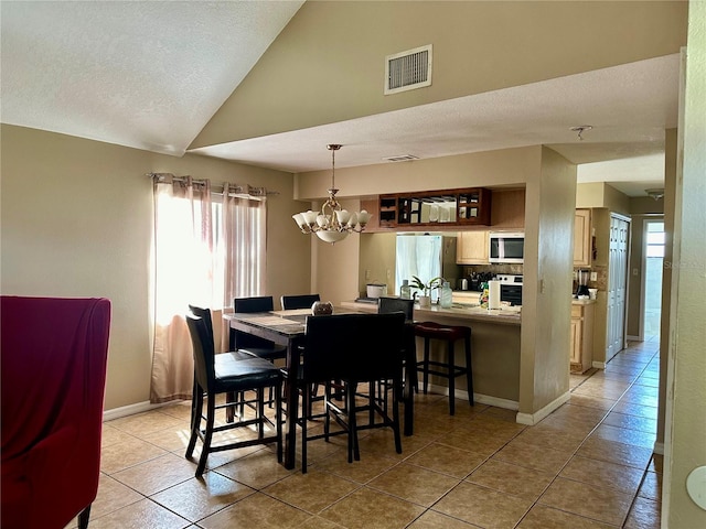 tiled dining room featuring vaulted ceiling, a textured ceiling, and an inviting chandelier