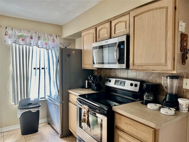 kitchen with decorative backsplash, a textured ceiling, light brown cabinetry, light tile patterned flooring, and stainless steel appliances