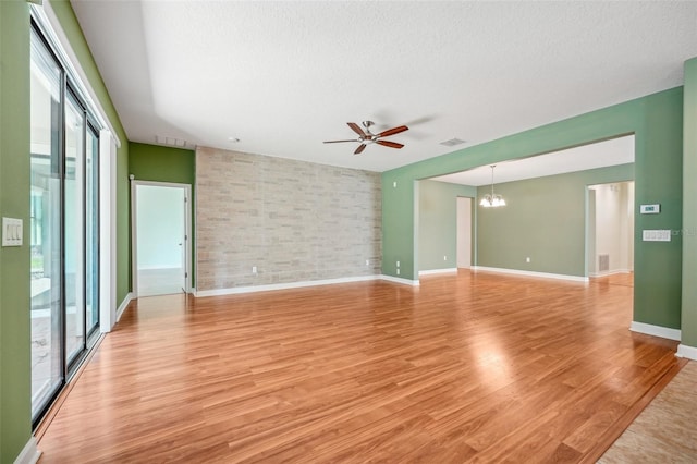 empty room with a textured ceiling, plenty of natural light, ceiling fan with notable chandelier, and light wood-type flooring