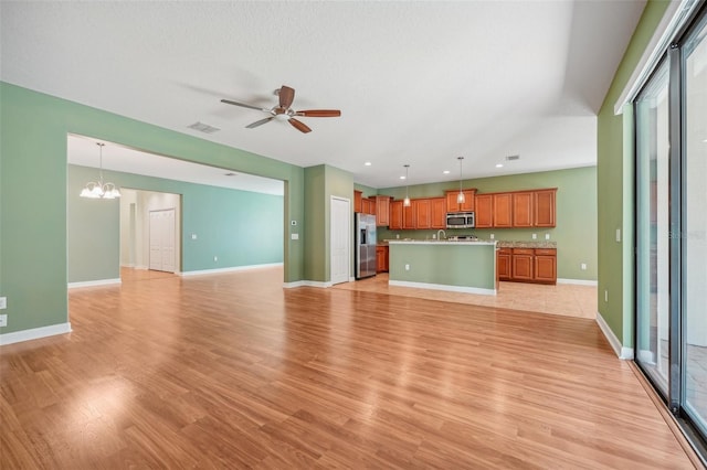 unfurnished living room with ceiling fan with notable chandelier, a textured ceiling, and light wood-type flooring