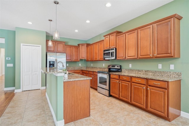 kitchen featuring sink, stainless steel appliances, light stone counters, decorative light fixtures, and a center island with sink