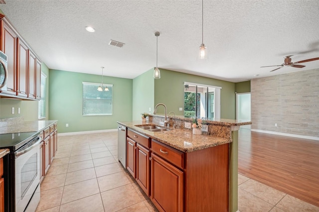 kitchen with stainless steel appliances, a kitchen island with sink, sink, light hardwood / wood-style floors, and hanging light fixtures