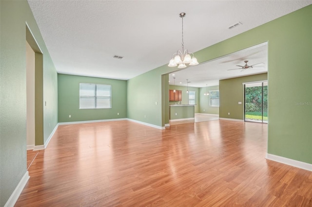 unfurnished room with a textured ceiling, ceiling fan with notable chandelier, and light hardwood / wood-style flooring