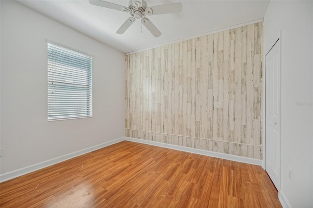 spare room featuring wood walls, ceiling fan, and wood-type flooring