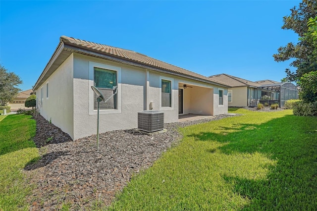 rear view of house featuring a lanai, ceiling fan, a yard, and cooling unit