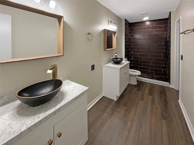 bathroom featuring hardwood / wood-style floors, tiled shower, vanity, and toilet