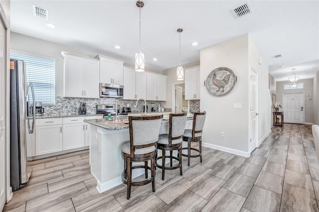 kitchen featuring stainless steel appliances, white cabinetry, light stone counters, and decorative light fixtures