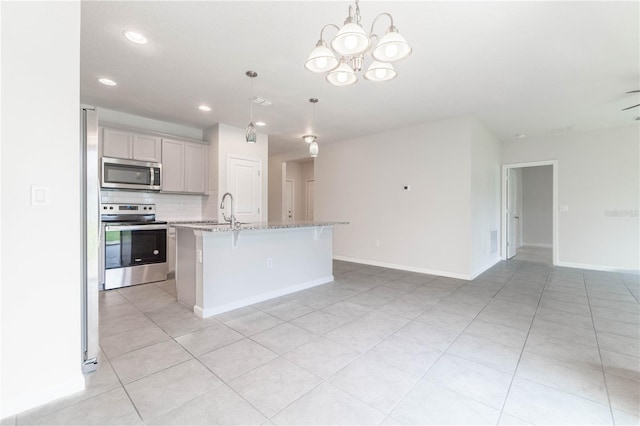 kitchen with sink, an island with sink, stainless steel appliances, pendant lighting, and light stone counters