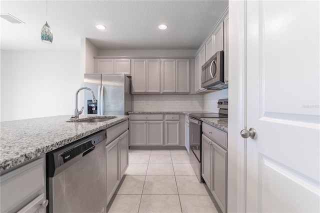 kitchen with gray cabinetry, stainless steel appliances, backsplash, sink, and light stone counters