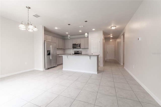 kitchen with a center island with sink, a kitchen bar, decorative light fixtures, appliances with stainless steel finishes, and light stone counters