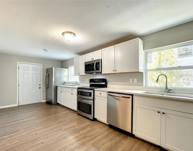 kitchen featuring light hardwood / wood-style flooring, sink, white cabinets, appliances with stainless steel finishes, and a textured ceiling