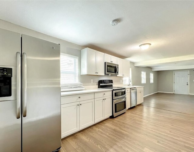 kitchen with appliances with stainless steel finishes, white cabinetry, sink, and light hardwood / wood-style floors