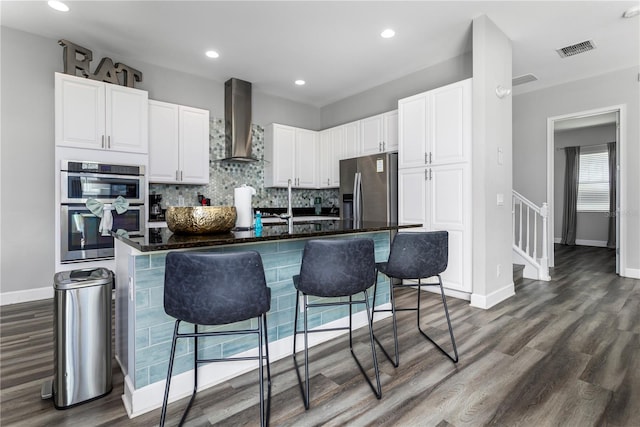 kitchen with wall chimney exhaust hood, white cabinets, appliances with stainless steel finishes, and a breakfast bar area