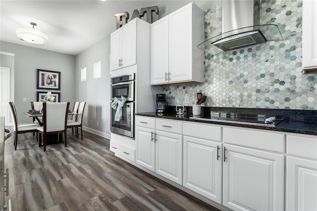 kitchen featuring wall chimney range hood, white cabinetry, stainless steel double oven, black cooktop, and dark hardwood / wood-style flooring