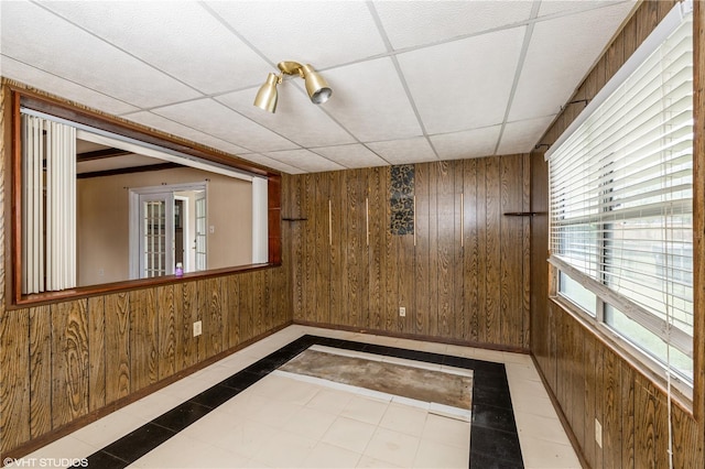 spare room with a paneled ceiling, wood walls, and light tile patterned floors