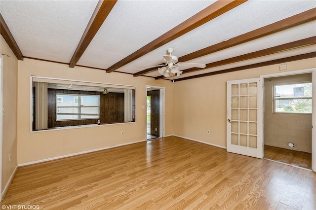 empty room featuring light hardwood / wood-style floors, beamed ceiling, a wealth of natural light, and a textured ceiling