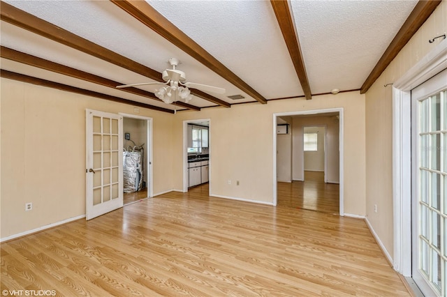 empty room with beamed ceiling, ceiling fan, french doors, light hardwood / wood-style floors, and a textured ceiling