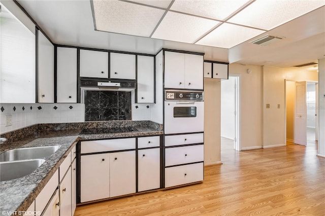 kitchen with black electric cooktop, tasteful backsplash, white cabinetry, light hardwood / wood-style flooring, and white oven