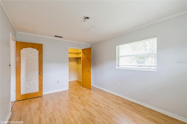 unfurnished bedroom with a spacious closet, light hardwood / wood-style floors, a closet, and ornamental molding