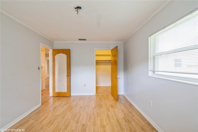 unfurnished bedroom with a closet, crown molding, a walk in closet, and light wood-type flooring