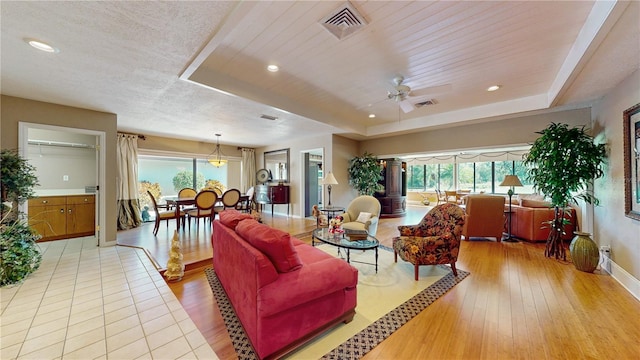 living room featuring light hardwood / wood-style flooring, a tray ceiling, and ceiling fan