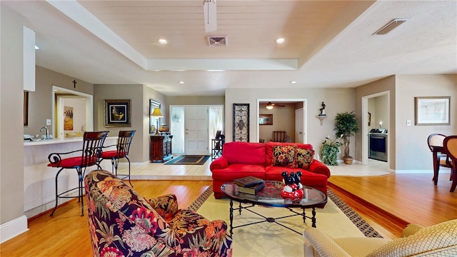 living room featuring ceiling fan, a raised ceiling, sink, and light wood-type flooring