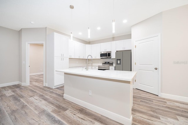 kitchen with pendant lighting, a kitchen island with sink, white cabinetry, stainless steel appliances, and light wood-type flooring