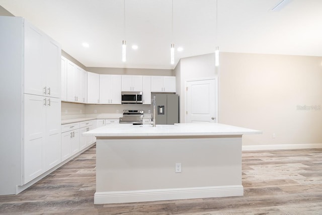 kitchen with an island with sink, decorative light fixtures, light hardwood / wood-style flooring, white cabinetry, and appliances with stainless steel finishes