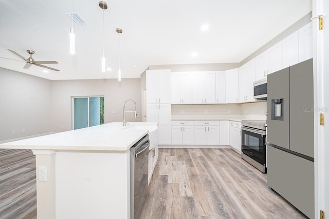 kitchen with an island with sink, stainless steel appliances, white cabinets, light hardwood / wood-style floors, and decorative light fixtures