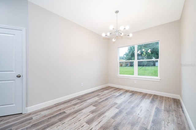 empty room featuring a notable chandelier and light wood-type flooring