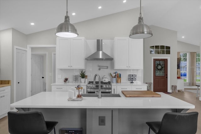 kitchen with an island with sink, high end stove, pendant lighting, lofted ceiling, and wall chimney range hood