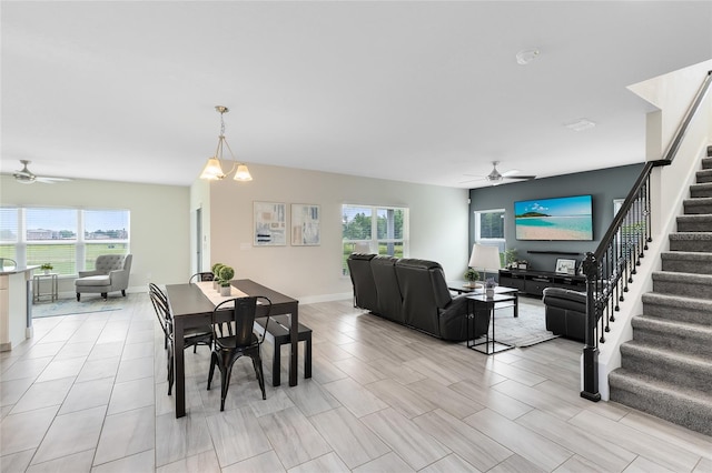 dining space featuring stairs, baseboards, a wealth of natural light, and ceiling fan with notable chandelier