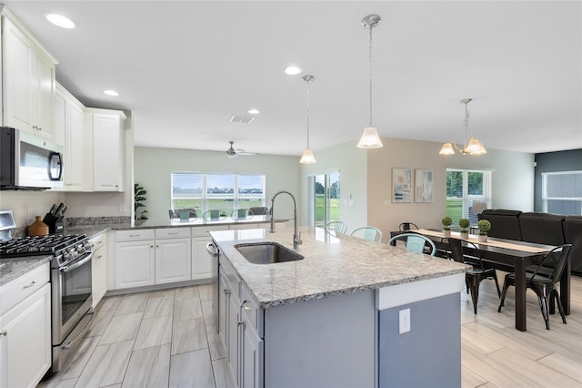 kitchen featuring appliances with stainless steel finishes, white cabinets, pendant lighting, a kitchen island with sink, and sink