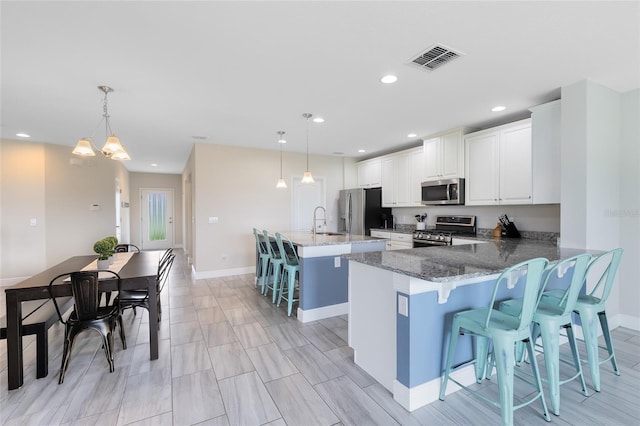 kitchen featuring appliances with stainless steel finishes, a breakfast bar, kitchen peninsula, decorative light fixtures, and dark stone counters