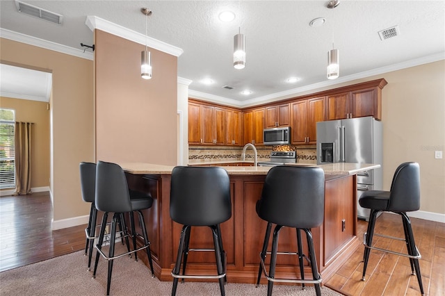 kitchen with appliances with stainless steel finishes, a breakfast bar, hardwood / wood-style flooring, and decorative light fixtures