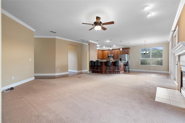 unfurnished living room with light carpet, a tile fireplace, crown molding, a textured ceiling, and ceiling fan with notable chandelier