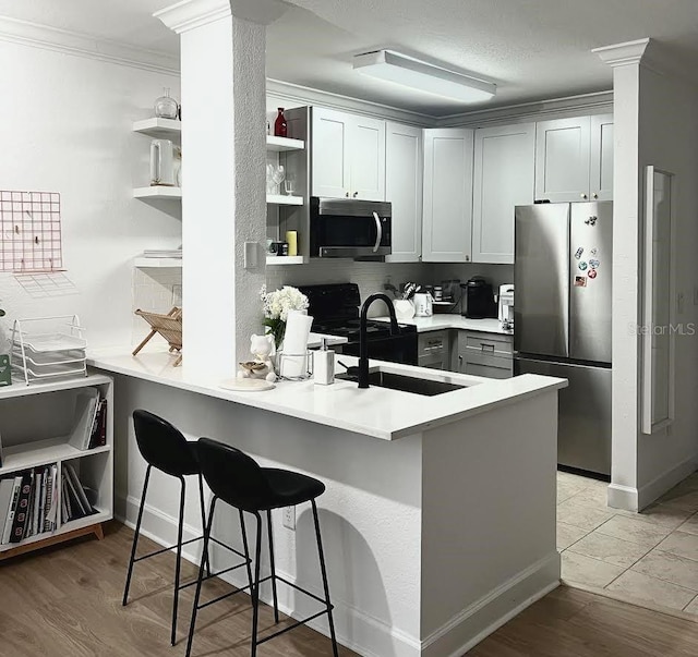 kitchen with gray cabinets, a breakfast bar area, appliances with stainless steel finishes, light hardwood / wood-style floors, and crown molding