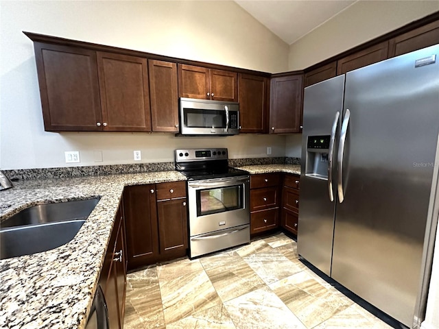 kitchen featuring light stone counters, dark brown cabinetry, sink, appliances with stainless steel finishes, and vaulted ceiling